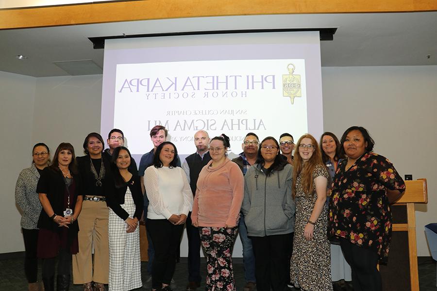 Members of Phi Theta Kappa standing in front presentation slide with Phi Theta Kappa Honor Society information