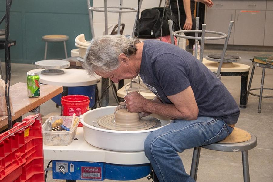 Adult students works on a potter's wheel in a Continuing Education class.