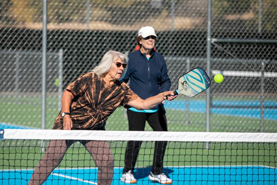 Female returns a serve playing Pickleball with her teammate at outdoor pickleball courts at Farmington's Brookside Park.