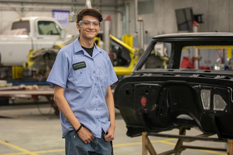 火博体育 student standing in front of a car frame in the auto body shop