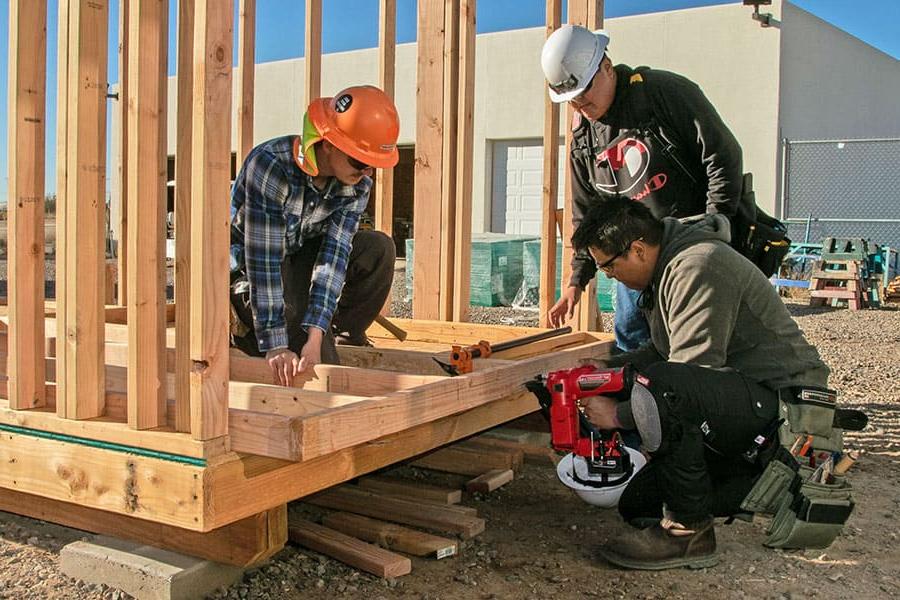 Two 火博体育 students with a professor building the frame for a wall