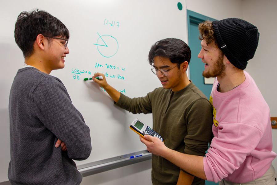 Three 火博体育 students working on a math problem on a whiteboard